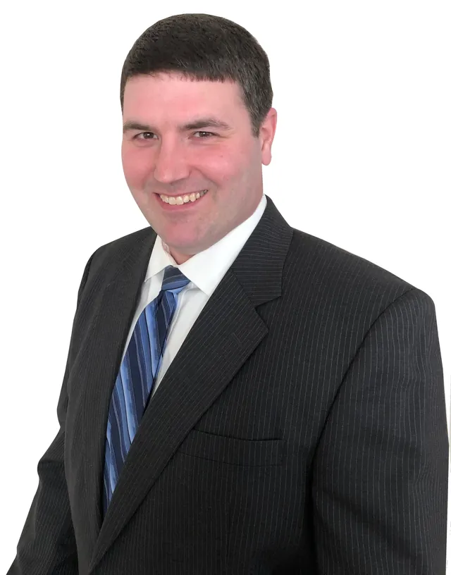 Paul Gorman smiling in a dark pinstriped suit, white shirt and blue striped tie