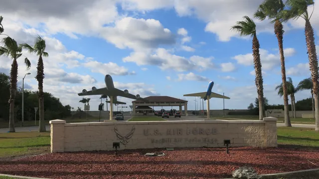 Entrance to MacDill Air Force Base: a U.S. Air Force sign, two aircraft on pylons, the gatehouse and palm trees under a cloudy blue sky