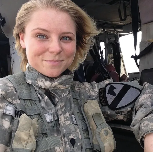Samantha Heller smiling in Army camouflage uniform and vest inside a helicopter cabin