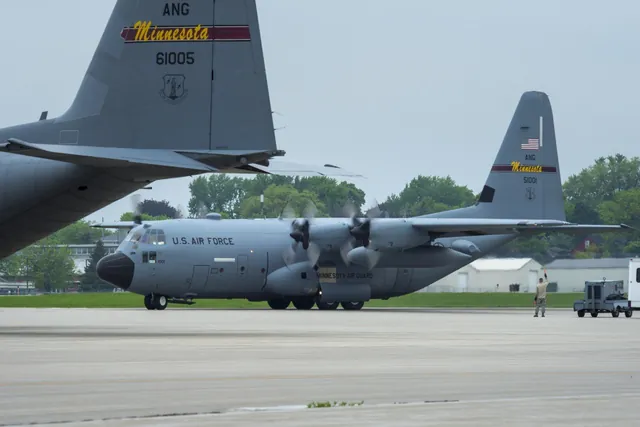 Two gray Minnesota Air National Guard C-130 Hercules aircraft on the flight line as a ground crew airman raises an arm toward the taxiing plane