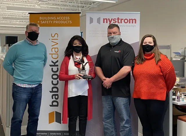 Matt Benson, Susan Aaker holding the eagle trophy, John Henka and Lindsey Jankowski, all masked, in front of Nystrom and Babcock Davis banners