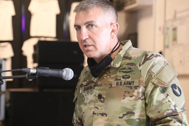Lt. Col. Chip Rankin in Army camouflage uniform, a face mask pulled down around his neck, speaking into a microphone