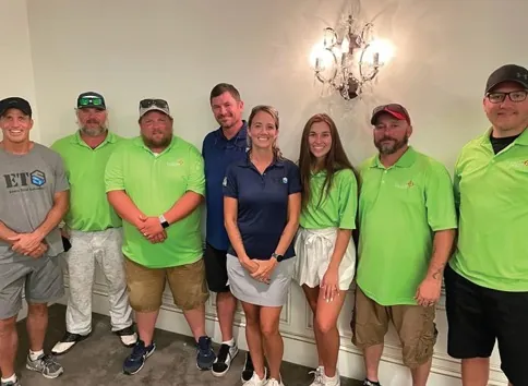 Eight golfers from the Every Third Saturday and LockLeed teams, most in lime green polos, posing together indoors beneath a wall chandelier.