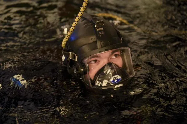 Coast Guard diver in a helmet and full face mask with only his head above the dark water of a frozen lake