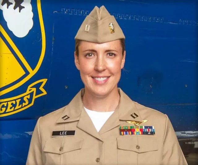 Lt. Amanda Lee smiling in Navy khakis and a garrison cap in front of a blue Blue Angels jet bearing the squadron crest