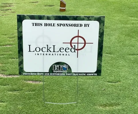 Camouflage-bordered golf course sign reading This Hole Sponsored By LockLeed International, with the Every Third Saturday logo