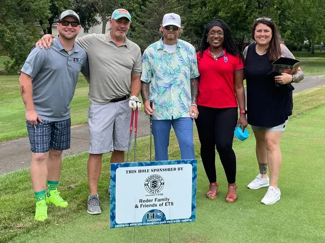 Five golfers smiling on a tee box behind a hole sign sponsored by the Reder Family and Friends of ETS