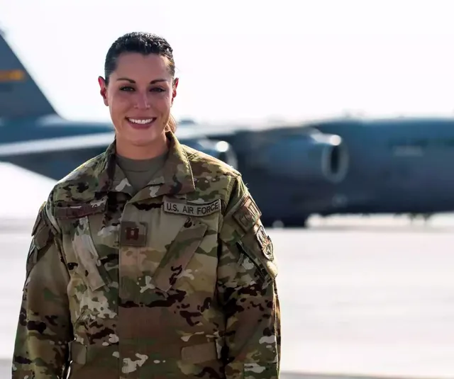 Katie Lunning smiling in Air Force camouflage uniform on a flight line, with a gray C-17 transport plane behind her.