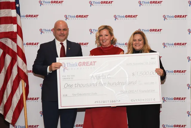 Erik Therwanger, Angela Cox and Jean Miller hold an oversized $1,500 Think GREAT Foundation check in front of a logo backdrop and a U.S. flag.