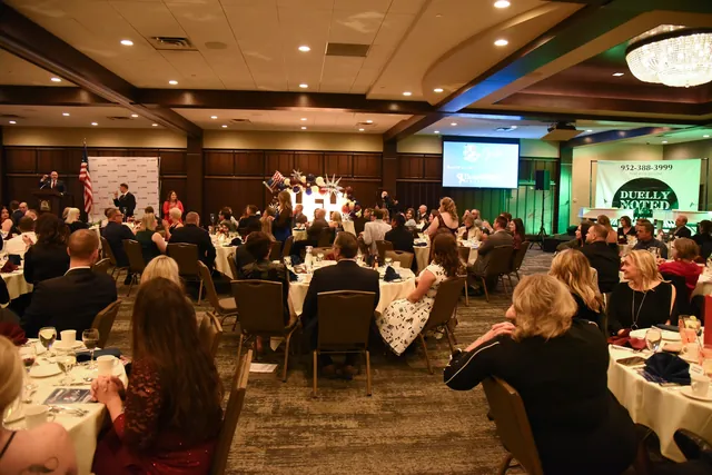 Guests at round banquet tables in a ballroom listen to a speaker at a podium, with the gala's Think GREAT logo on a screen.