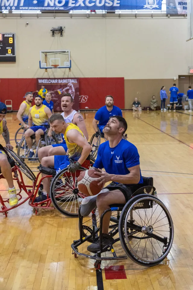 Brandon Sullivan, in a blue Air Force Wounded Warrior shirt, looks up at the hoop with the ball during a wheelchair basketball game