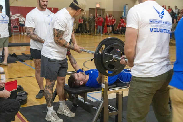 Brandon Sullivan lies on a bench and presses a loaded barbell while Air Force Wounded Warrior volunteers spot him