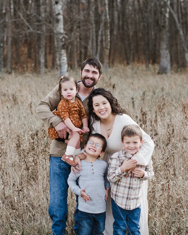 Brandon Sullivan, his wife Valeria and their three children pose together in a field of tall autumn grass