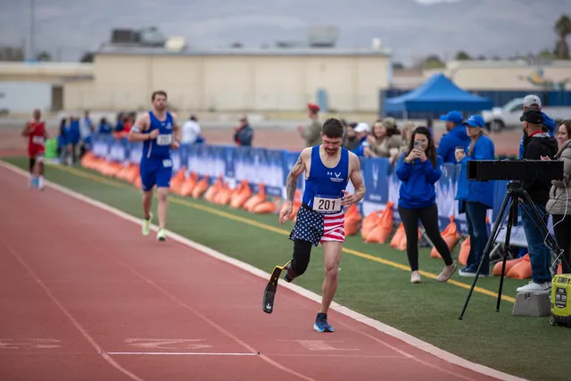 Brandon Sullivan, wearing bib 201, stars-and-stripes shorts and a running blade, sprints down the track as spectators watch