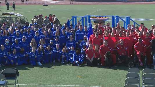 Athletes in blue and in red team uniforms gather for a group photo on a sports field at the 2024 Air Force and Marine Corps Trials