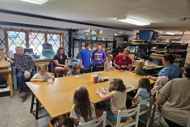 Children, teens and adults seated around a large table in a workshop, working on a craft project together