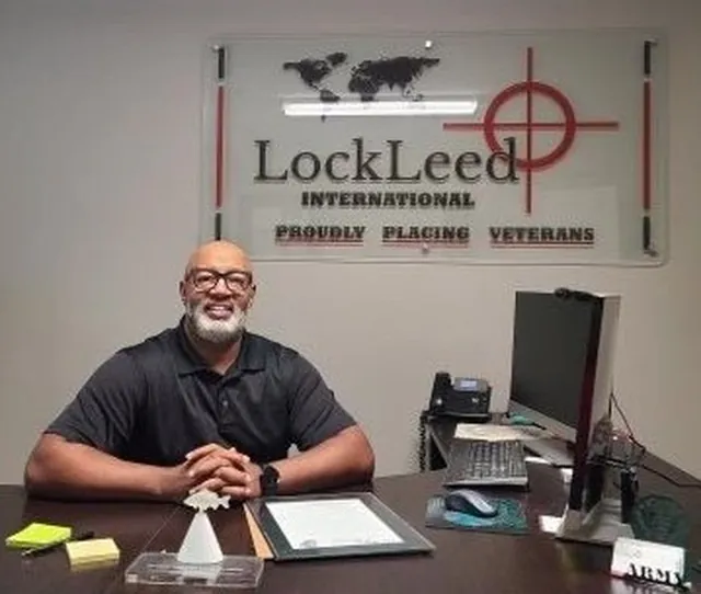 Jim Walker smiling at his desk in front of a LockLeed International Proudly Placing Veterans sign