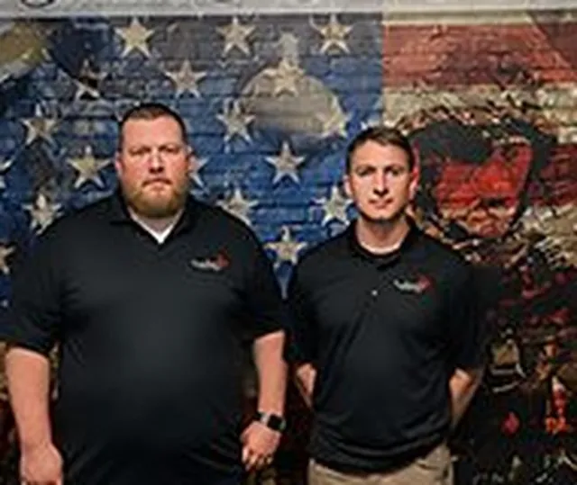 Two LockLeed team members in black polo shirts in front of a painted American flag mural